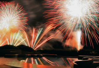 Colorati fuochi d’artificio illuminano la notte sopra Camping Union Lido Mare in Veneto, Italia, visti dalla piscina.