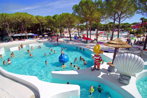 Famiglie si divertono in piscina e nell'area solarium tra gli alberi al Camping Union Lido Mare in Veneto, Italia.