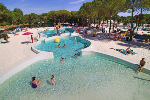 Famiglie si rilassano tra piscina e spiaggia sabbiosa al Camping Union Lido Mare, un villaggio in Veneto.
