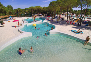 Familier nyder poolen og sandstranden omgivet af træer på Camping Union Lido Mare-feriepark i Veneto.