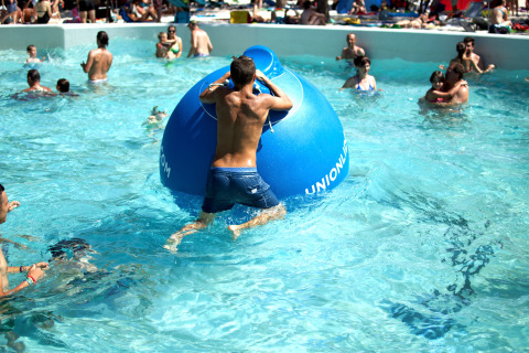 People enjoying the swimming pool and playing with a large blue inflatable at Camping Union Lido Mare, Italy.