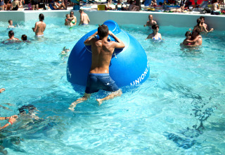 Mennesker nyder poolen og leger med en stor blå oppustelig bold i Camping Union Lido Mare, Veneto, Italien.