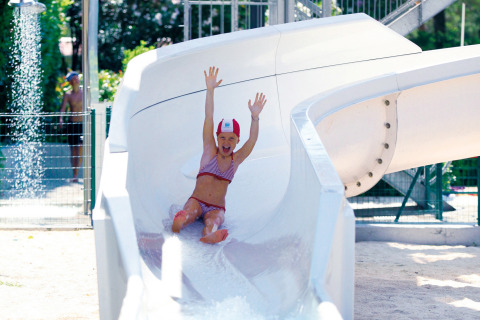 Bambina in costume scivola su uno scivolo d'acqua a Camping Union Lido Mare, parco vacanze in Veneto.