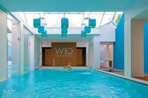 Piscina interior en W10 Leisure Building de Camping Union Lido Mare, Véneto, Italia, con diseño moderno y azul.