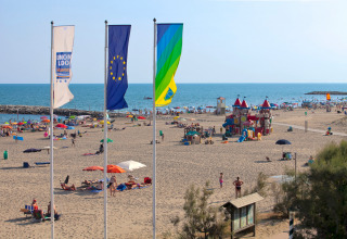 Travl strand ved Camping Union Lido Mare i Veneto, Italien, med farverige paraplyer og legeplads nær havet.