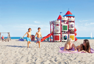 Børn leger på stranden ved Camping Union Lido Mare i Veneto, Italien, med farverigt legepladsudstyr.