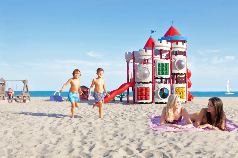 Kinderen spelen op het strand bij Camping Union Lido Mare in Veneto, Italië, met kleurrijke speeltoestellen.