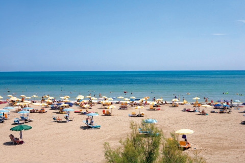 Beach scene at Camping Union Lido Mare in Veneto, Italy, showing umbrellas, lounge chairs, and sunbathers.