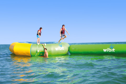Niños jugando en un parque acuático inflable Wibit en Camping Union Lido Mare, Véneto, Italia, bajo el sol.