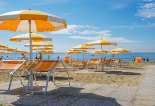 Zonnige ligstoelen en parasols op het strand bij Camping Union Lido Mare in Veneto, Italië.