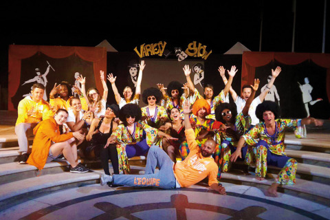 Gruppo festoso in costumi colorati posa sui gradini durante uno show al Union Lido Mare, Veneto, Italia.