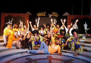 Joyful group in colorful costumes posing on steps during a Variety Show at Union Lido holiday park, Italy.