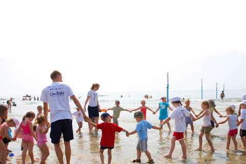 Bambini e adulti giocano in cerchio sulla spiaggia al Camping Union Lido Mare, villaggio vacanze in Veneto, Italia.