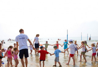 Bambini e adulti giocano in cerchio sulla spiaggia al Camping Union Lido Mare, villaggio vacanze in Veneto, Italia.