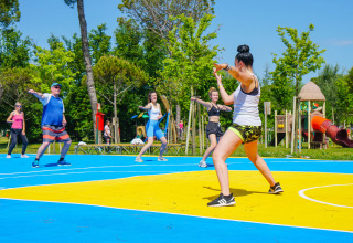 En gruppe mennesker deltager i en udendørs fitnessklasse på farverigt underlag i Camping Union Lido Mare i Veneto, Italien.