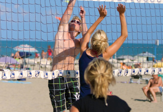 Mensen spelen beachvolleybal op het zandstrand bij Camping Union Lido Mare in Veneto, Italië, op een zonnige dag.