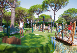 Børn spiller minigolf på en grøn bane med træer og broer ved Camping Union Lido Mare i Veneto, Italien.