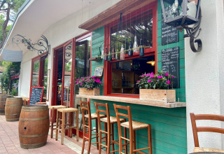 Outdoor bar area at Camping Union Lido Mare, Veneto, Italy with high stools, wine barrels, and flowers.