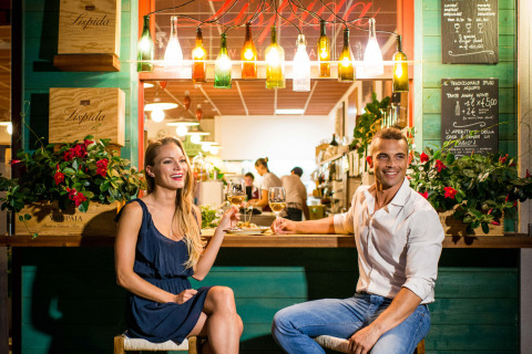 Una pareja sonriente disfruta vino en un bar colorido del Camping Union Lido Mare en Véneto, Italia.