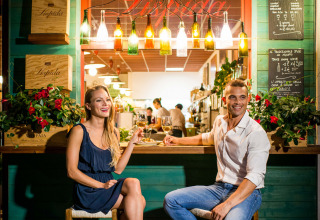 Una pareja sonriente disfruta vino en un bar colorido del Camping Union Lido Mare en Véneto, Italia.