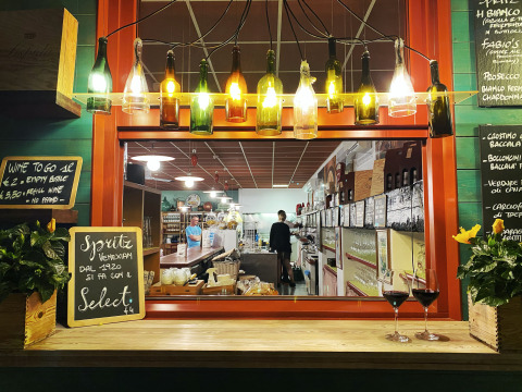 Wine bar with hanging bottle lamps, flowers, and chalkboard menus at a holiday park in Veneto, Italy at night.