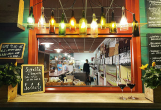 Wine bar with hanging bottle lamps, flowers, and chalkboard menus at a holiday park in Veneto, Italy at night.