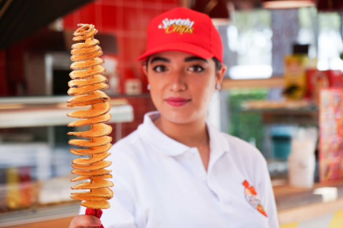 Mujer con gorra roja sostiene una brocheta de papa espiral en Camping Union Lido Mare, Véneto, Italia.