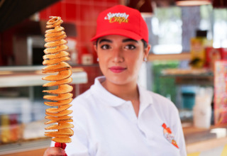 Donna con cappellino rosso tiene uno spiedino di patate a spirale a Camping Union Lido Mare, Veneto, Italia.