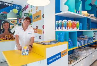 Employée dans la boutique Union Lido d’un camping en Vénétie, Italie, entourée de souvenirs colorés.
