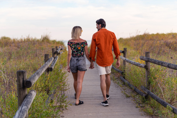 Couple walking hand in hand on a wooden path at Camping Union Lido Mare in Veneto, Italy.