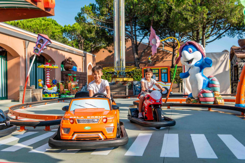 Niños disfrutan de atracciones en mini autos y motos en Camping Union Lido Mare, Veneto, Italia.