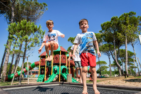 Bambini che giocano e saltano sul trampolino nel parco giochi di Camping Union Lido Mare, Veneto, Italia.