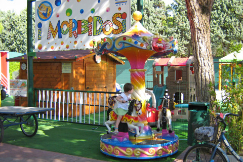 Carrusel infantil en Camping Union Lido Mare, parque vacacional en Véneto, Italia, rodeado de juegos y árboles.