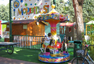 Børnekarrusel ved Camping Union Lido Mare i Veneto, Italien, omgivet af legeområde og grønne træer.