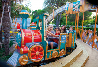 Familie nyder en farverig mini-tog-forlystelse på Camping Union Lido Mare feriepark i Veneto, Italien.