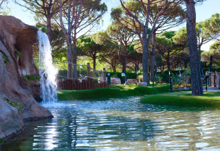 Cascada y estanque rodeados de árboles en el Camping Union Lido Mare, parque vacacional en Véneto, Italia.
