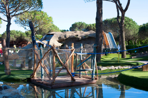 Campo de mini golf en Camping Union Lido Mare, Véneto, Italia, con puente colgante y paisaje rocoso.
