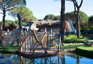 Campo da mini-golf al Camping Union Lido Mare in Veneto, Italia, con ponte sospeso e grotta artificiale.