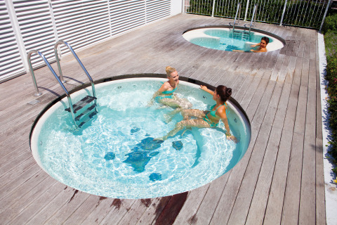 Three people relax in outdoor whirlpool tubs at Camping Union Lido Mare holiday park in Veneto, Italy.