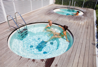 Three people relax in outdoor whirlpool tubs at Camping Union Lido Mare holiday park in Veneto, Italy.