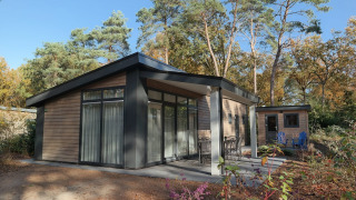 Forest park chalet 8p en Holiday park De Kleine Belties, Países Bajos, rodeado de árboles del bosque.