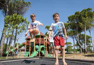To drenge leger og hopper på en legeplads ved Camping Union Lido Mare, omgivet af træer i Veneto, Italien.