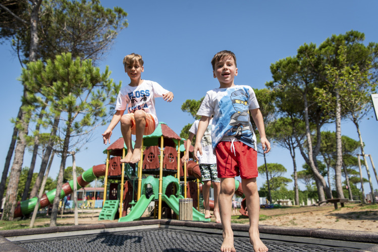 Two boys are playing and jumping on a playground trampoline at Camping Union Lido Mare in Veneto, Italy.