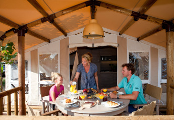 Family enjoying breakfast together at a table in a glamping tent with a covered outdoor veranda area.