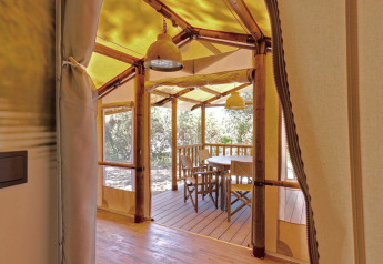 Interior view of a glamping tent with wooden table and chairs, overlooking a deck and surrounding nature.