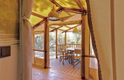 Vista interior de una tienda glamping con mesa y sillas de madera en una terraza rodeada de naturaleza.