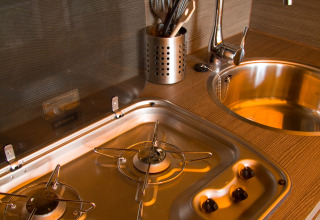 Angolo cucina moderno da glamping con fornello a gas, lavello tondo e utensili su piano in legno.