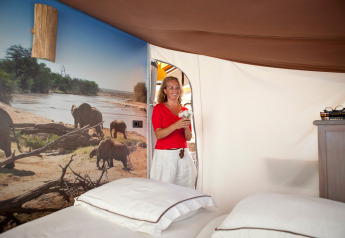 Woman in red enters cozy glamping tent bedroom with twin beds and elephant mural on the wall.