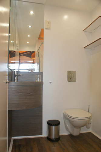 Modern bathroom at glamping accommodation with wall-mounted toilet, sink, large mirror, and wood flooring.