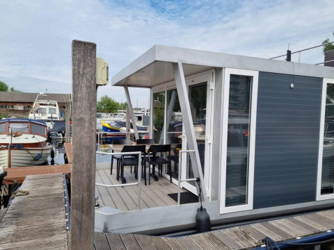 Casa flotante moderna 'De Hoop' en Marina Parcs - Jachthaven De Hoop, Países Bajos, con terraza y sillas.